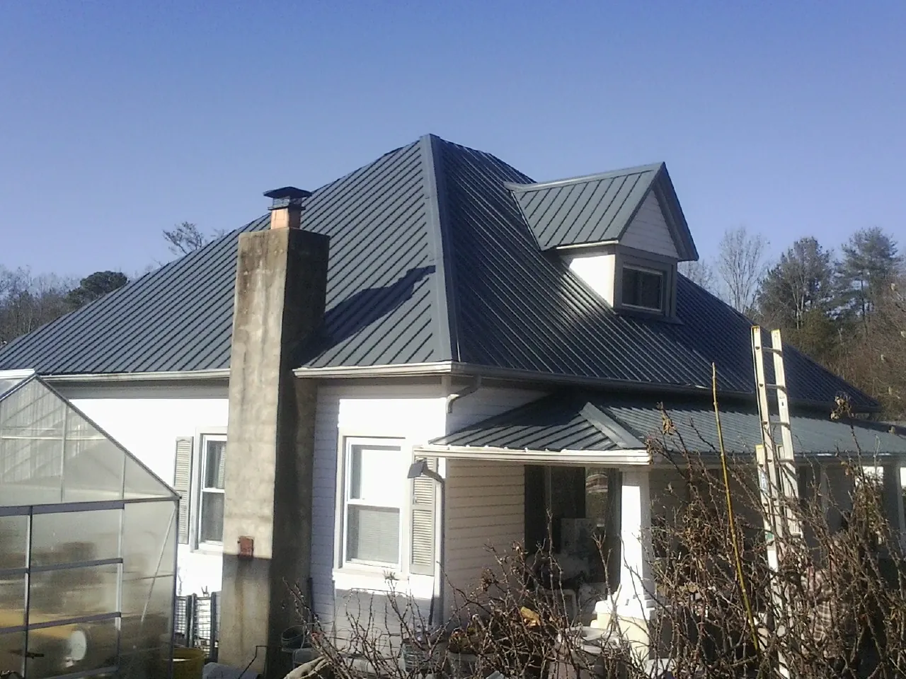 Dark blue standing seam metal roof on a white farmhouse with dormer — Slate & Tile Roof Repair by Roofing Brothers in East Lynne
