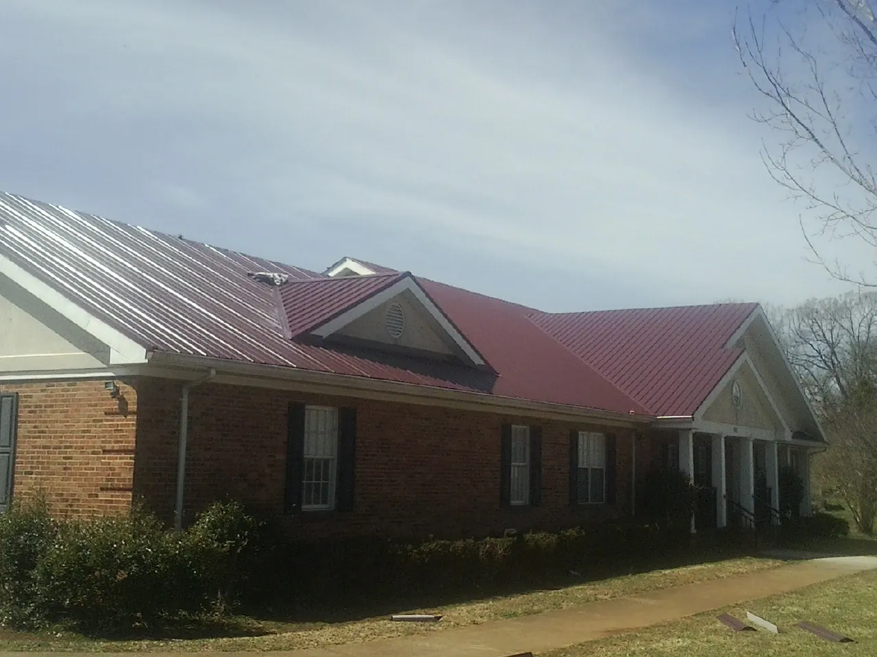 Red metal roof with gabled entries on a long brick building, from a Hail Damage Roof Repair job in East Lynne
