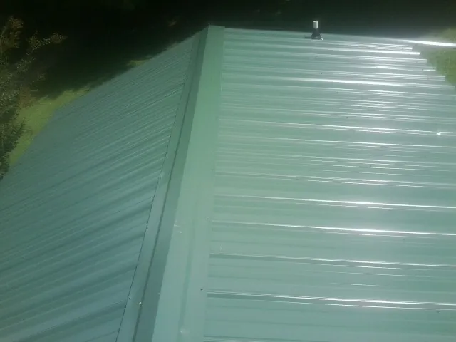 New green metal panels meeting at the ridge of a roof — Flat Roof Repair work by our crew in East Lynne