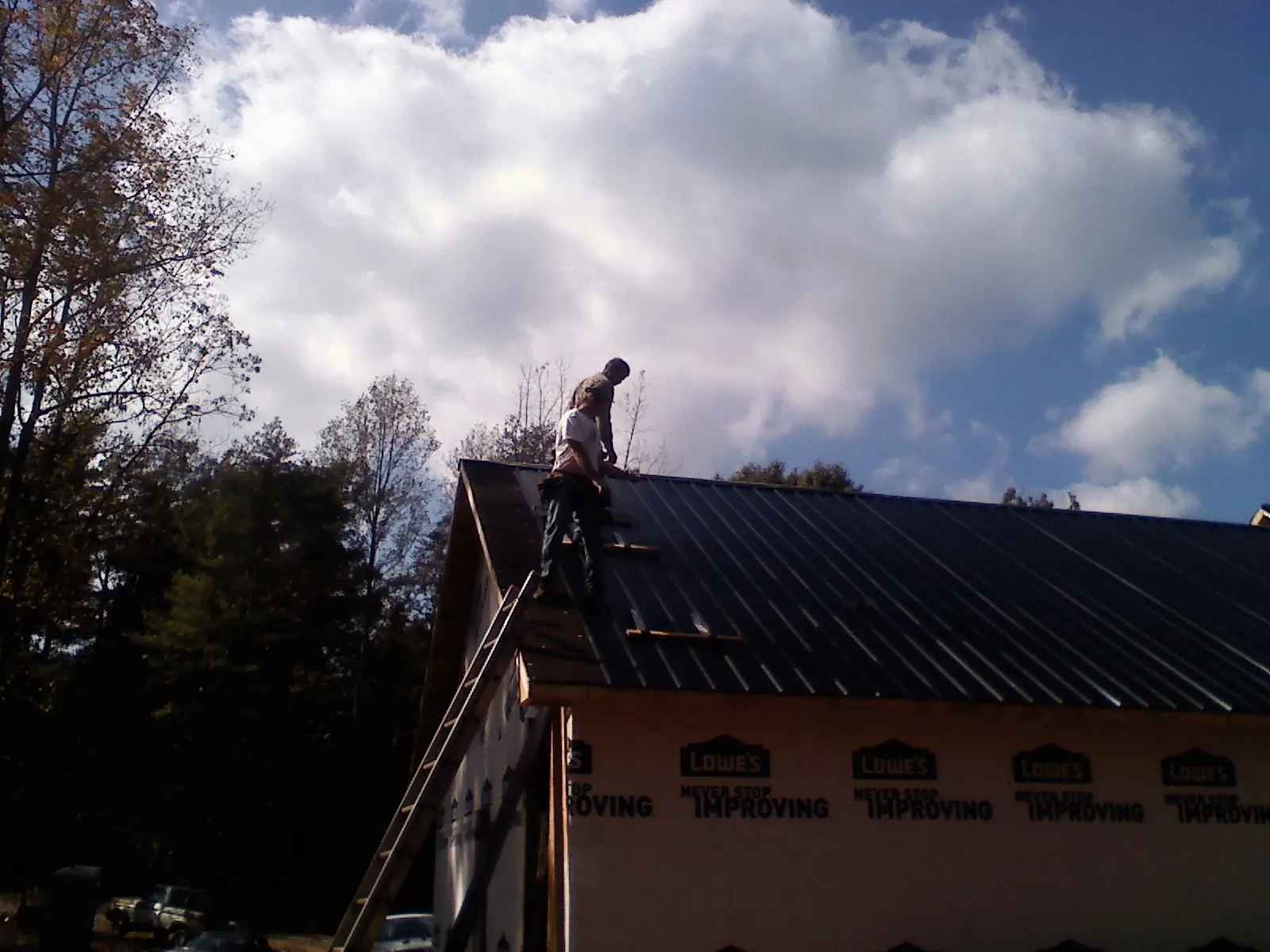 Roofer fastening dark metal panels high against a cloudy sky, from a Roof Inspection job in East Lynne