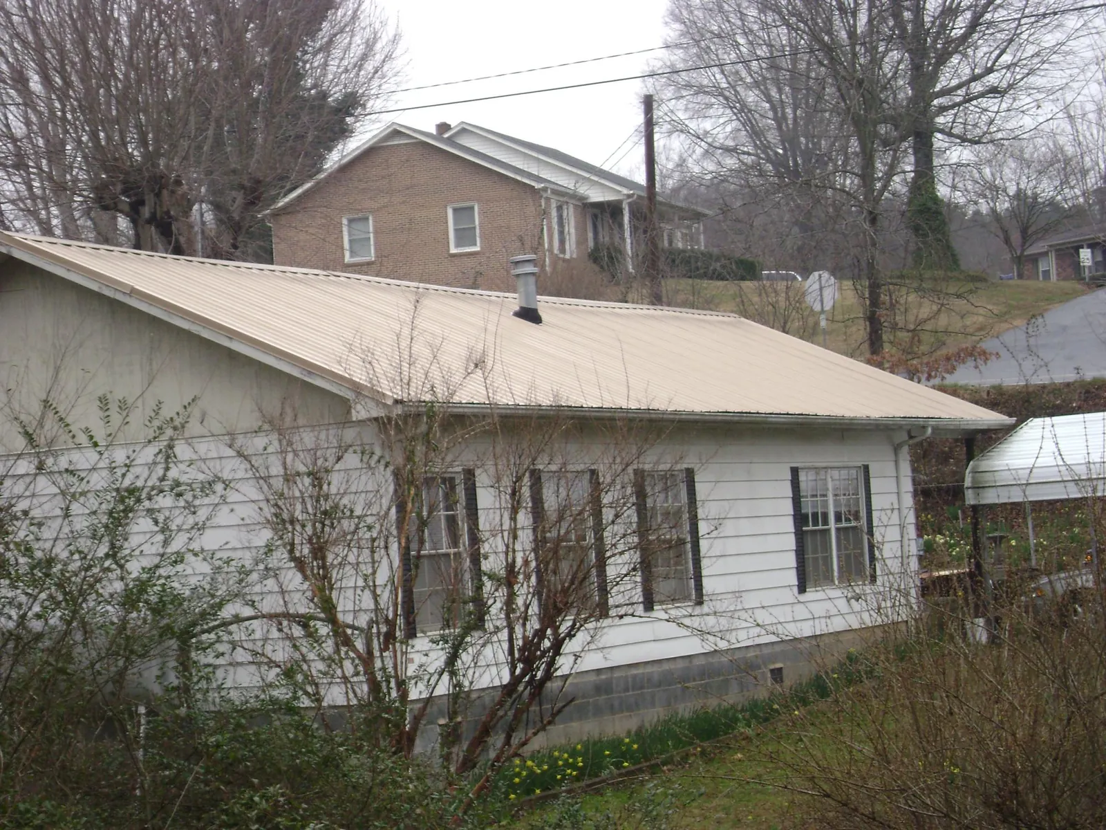 Tan metal roof on a white sided house set into a hillside — Commercial Roofing by Roofing Brothers in East Lynne